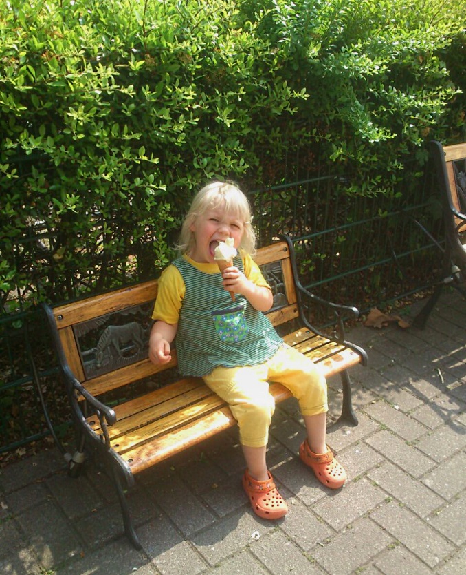 Child eats ice cream sat on park bench